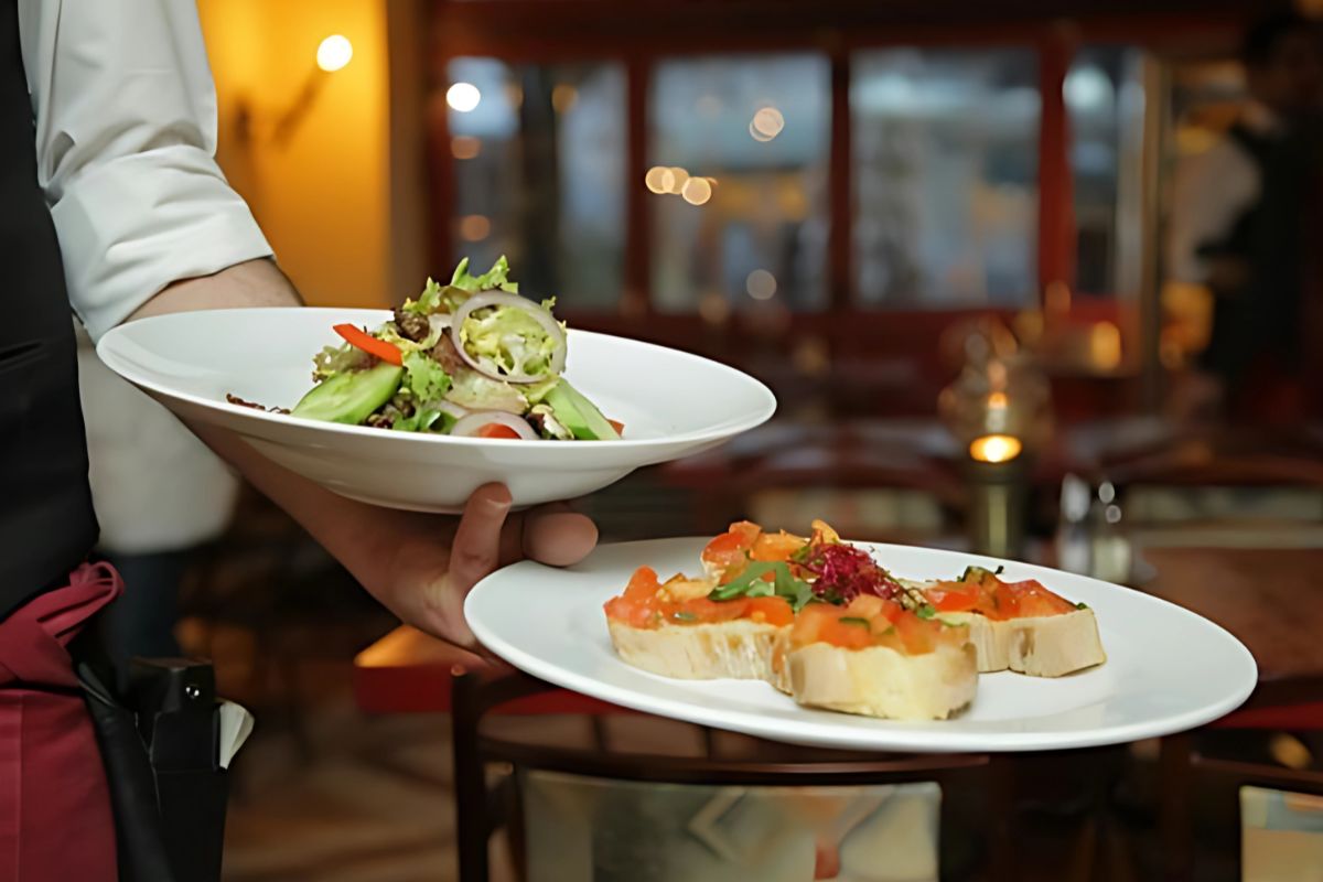 a waiter holding food plates - top dinner places in central london