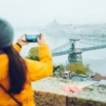 a girl clicking picture of a bridge in Budapest